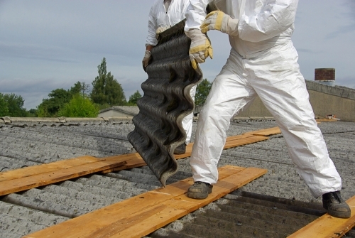  Professionelle haandvaerkere i beskyttelsesdragter fjerner et asbesttag sikkert. Arbejdet udfoeres med forsigtighed for at undgå spredning af asbestfibre.